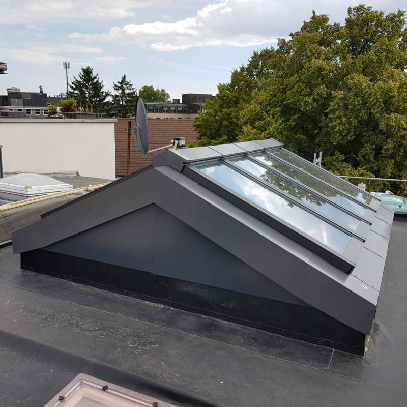 Eine große Lichtkuppel in Form eines Zeltdaches mit Dachfenstern auf einem Flachdach.